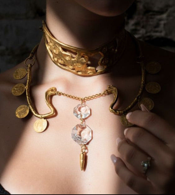 Close-up of a person wearing an ornate gold necklace with coins and a pendant.
