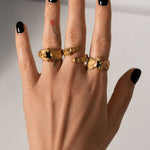 Gold ring with an emerald gemstone on a hand  styled with multipe rings- The Bow Jewelry