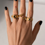 Gold ring with an emerald gemstone on a hand  styled with multipe rings- The Bow Jewelry
