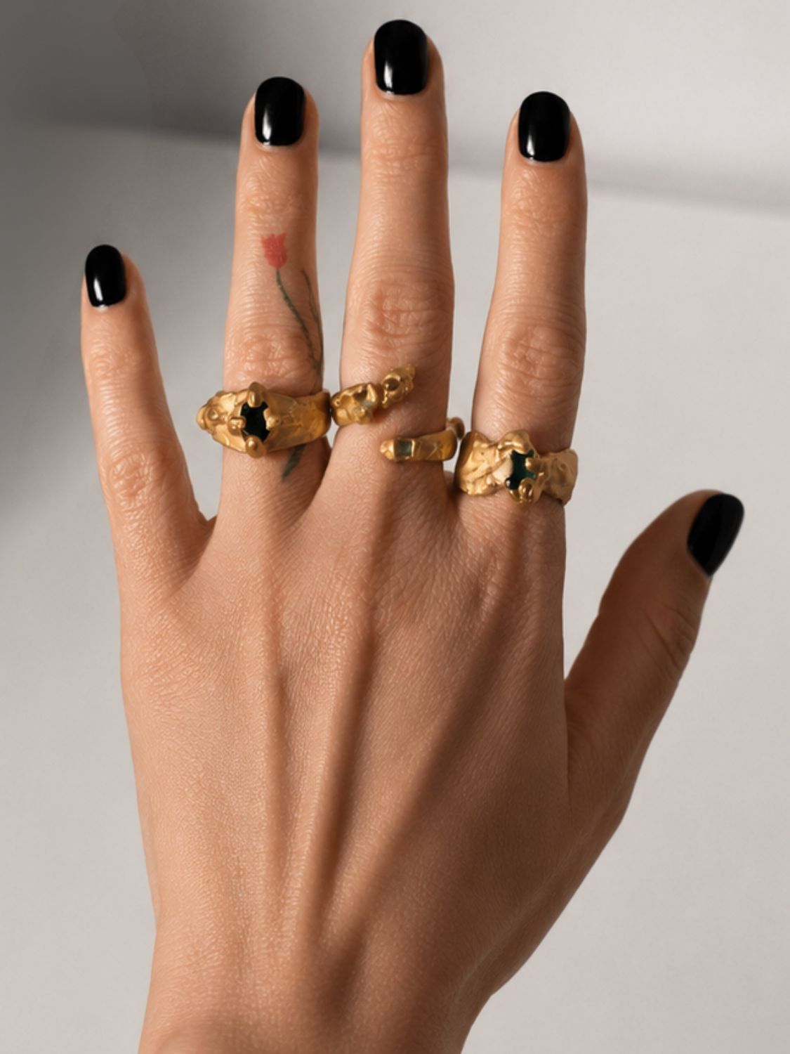 Gold ring with a emerald gemstone on a hand styled with multiple rings- The Bow Jewelry