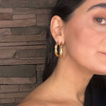 Close-up of a woman wearing goddess gold hoop earrings with a stone wall background