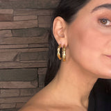 Close-up of a woman wearing goddess gold hoop earrings with a stone wall background