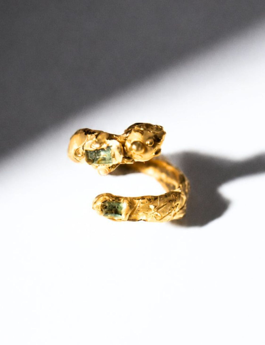 Gold snake shaped ring with two emerald gemstones on a white background - The Bow Jewelry