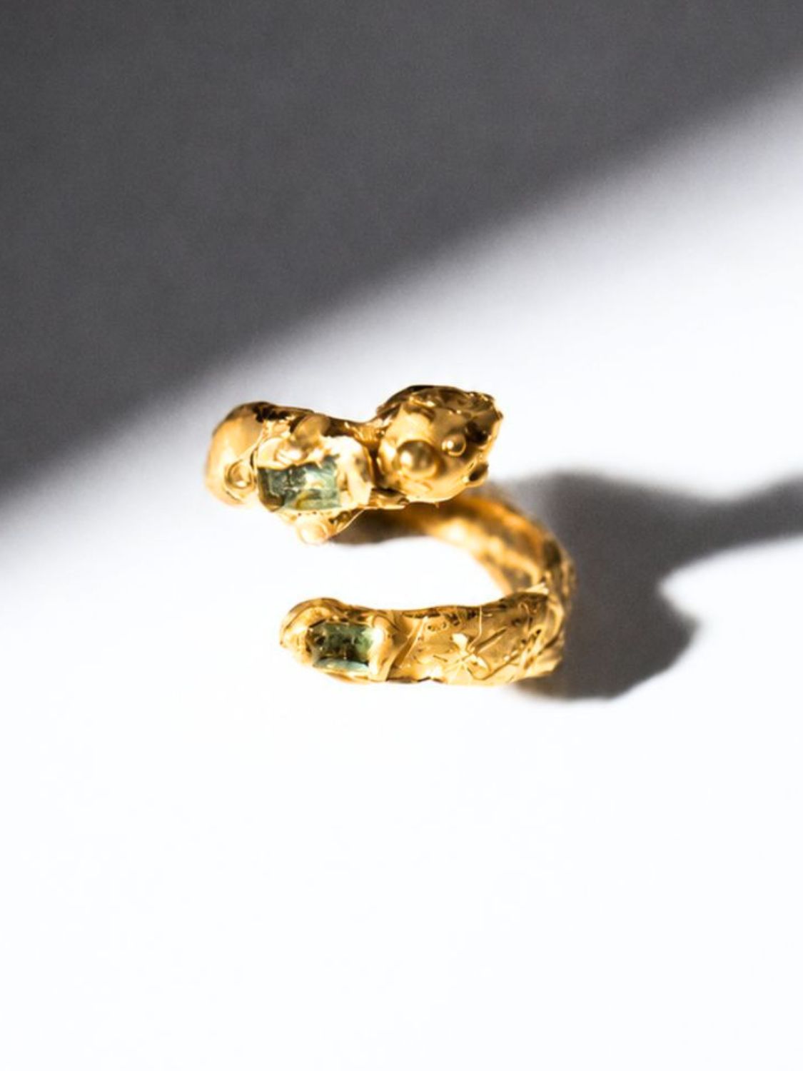 Gold snake shaped ring with two emerald gemstones on a white background - The Bow Jewelry