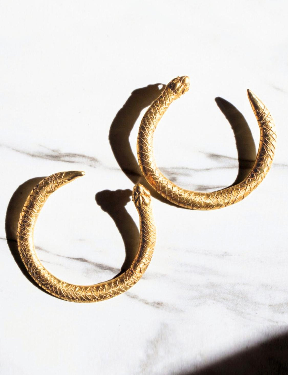 Gold Serpent Ouroboros hoop earrings on a white marble surface | The Bow Jewelry