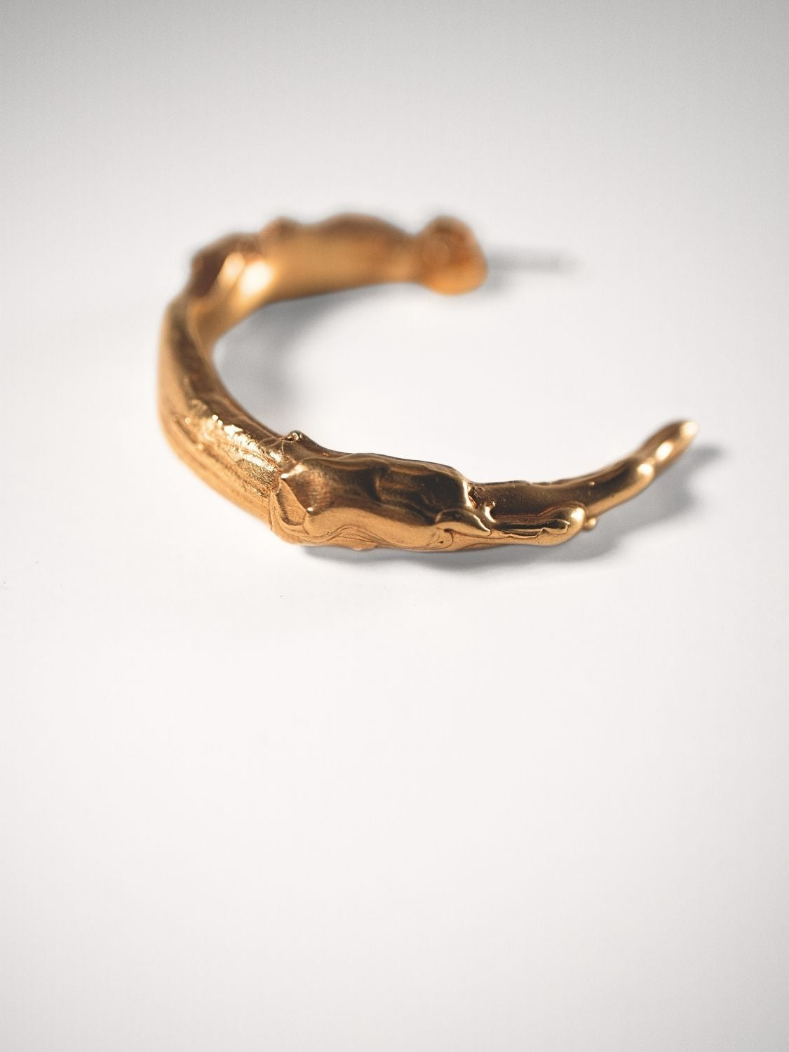 Gold sculptural hoops on a light grey background