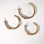 Three sculptural goddess gold hoop earrings on a light grey background