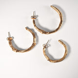 Three sculptural goddess gold hoop earrings on a light grey background
