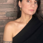 Woman wearing a black top with sculptural gold hoops against a stone wall background