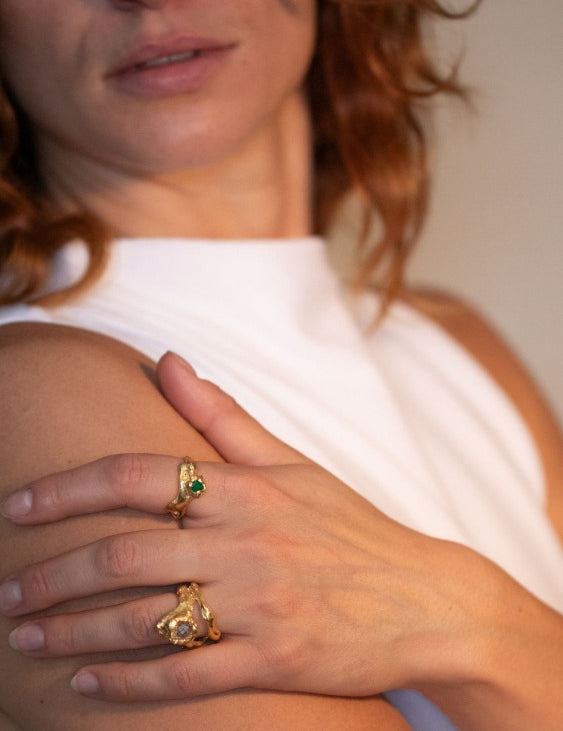 A gold-plated, tear-shaped emerald ring with a metallic band and a single emerald gemstone in the center on model. | The Bow Jewelry