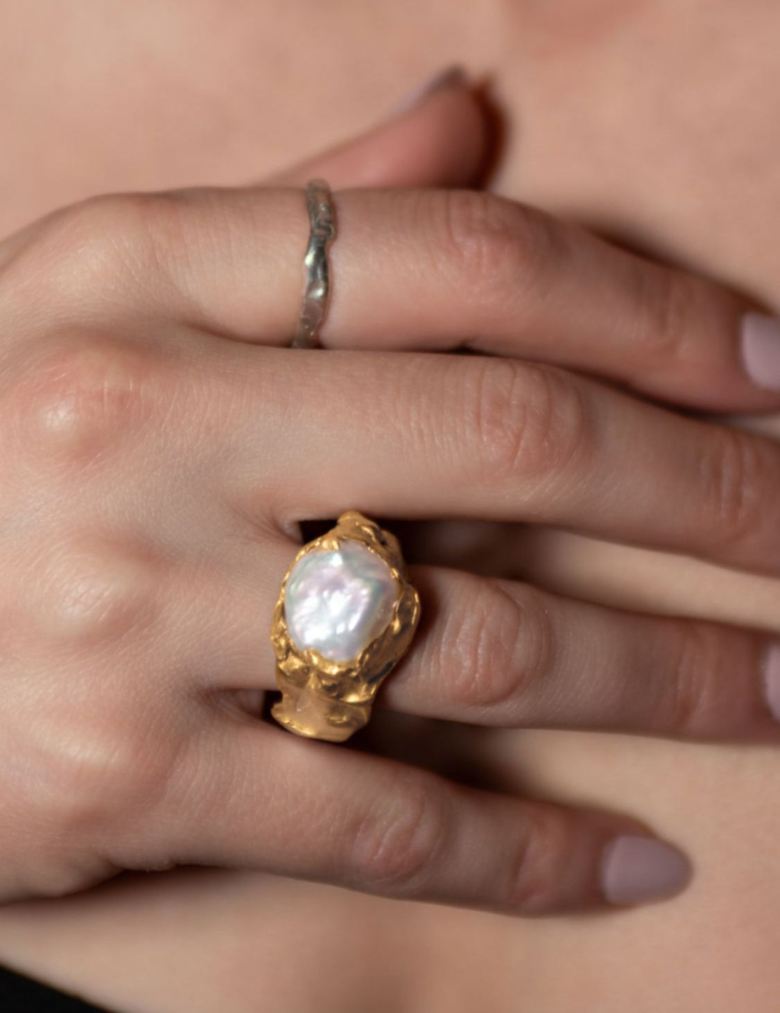 Gold ring with a pearl on a hand against a neutral background