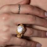 Gold ring with a pearl on a hand against a neutral background