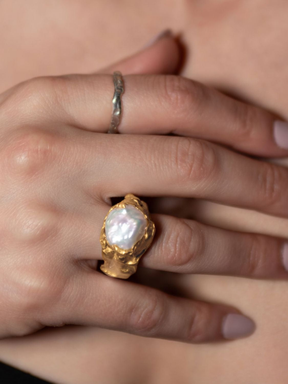 Gold ring with a pearl on a hand against a neutral background