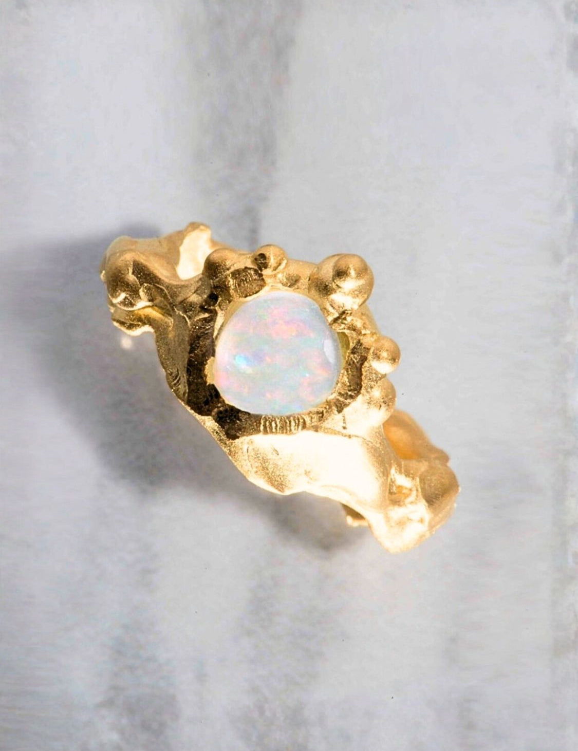 Gold ring with a central opal stone on a light gray background