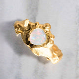 Gold ring with a central opal stone on a light gray background