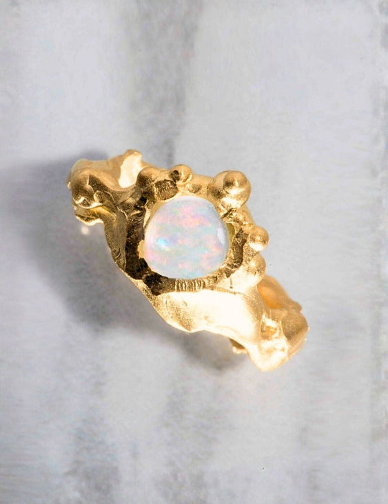Gold ring with a central opal stone on a light gray background