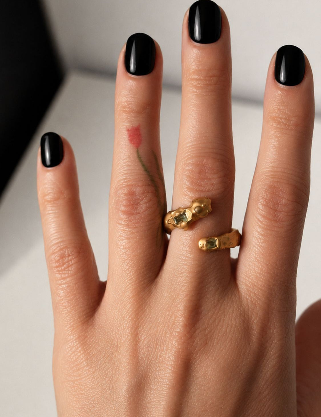 Gold snake shaped ring with two emerald gemstones on a hand - The Bow Jewelry