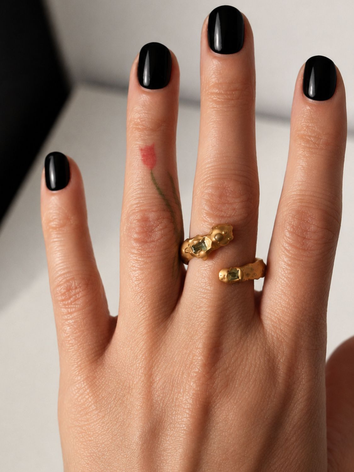 Gold snake shaped ring with two emerald gemstones on a hand - The Bow Jewelry