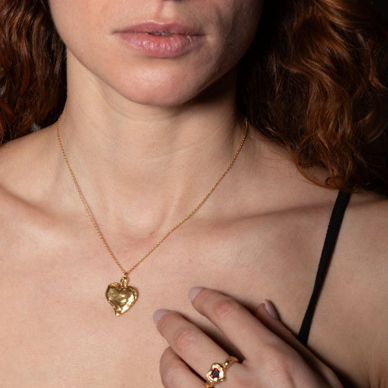 A model wearing gold-plated Heart shaped ring with a pear-shaped garnet in the center, set in a heart shape | The Bow Jewelry