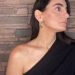 Woman wearing a black top with sculptural gold hoops against a stone wall background