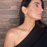 Woman wearing a black top with sculptural gold hoops against a stone wall background