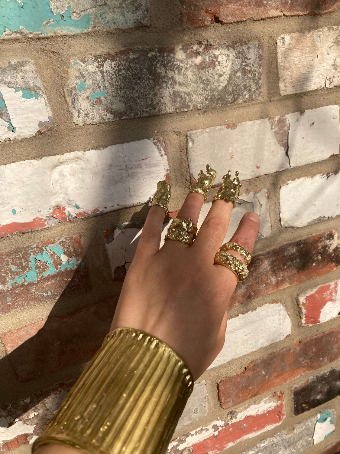 Hand wearing gold rings with a textured brick wall background