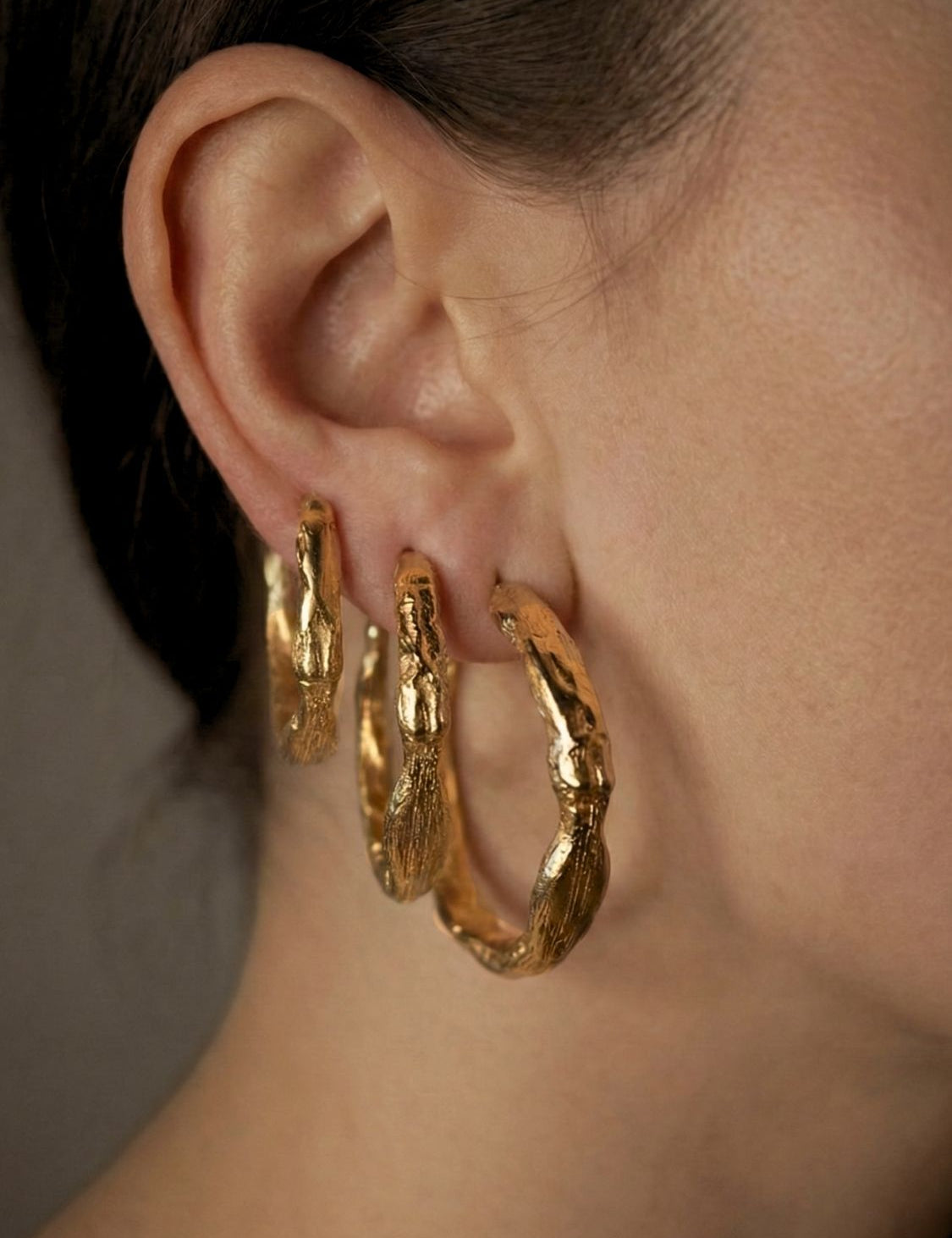 Sculptural gold hoop earrings worn by a person with a neutral background