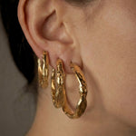Sculptural gold hoop earrings worn by a person with a neutral background