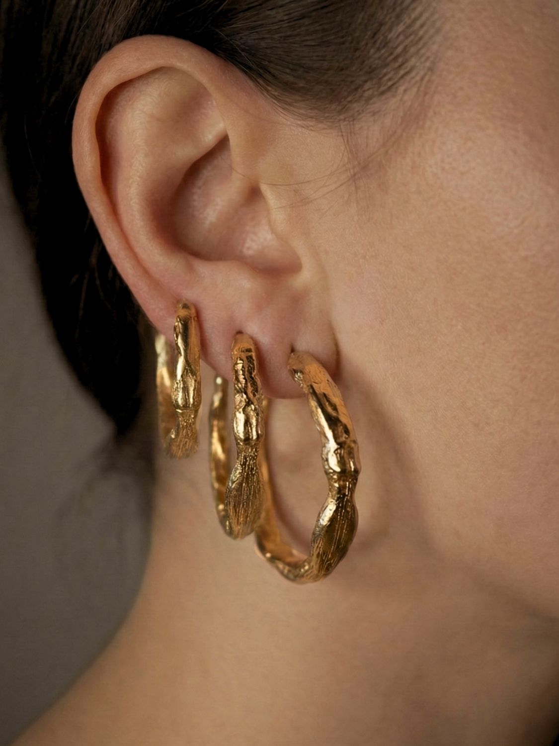 Sculptural gold hoop earrings worn by a person with a neutral background