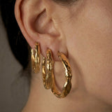 Sculptural gold hoop earrings worn by a person with a neutral background