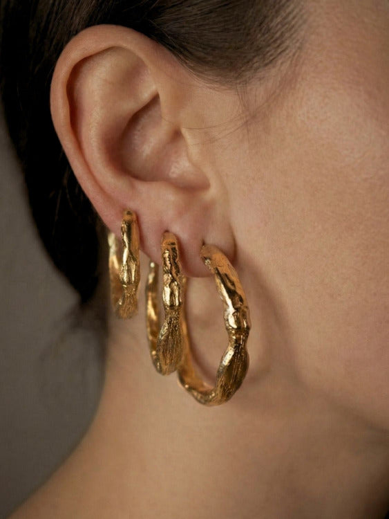 Sculptural gold hoop earrings worn by a person with a neutral background