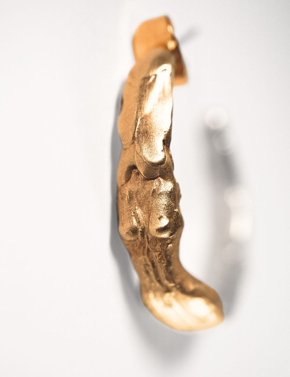 Gold goddess-shaped earring on a light grey background
