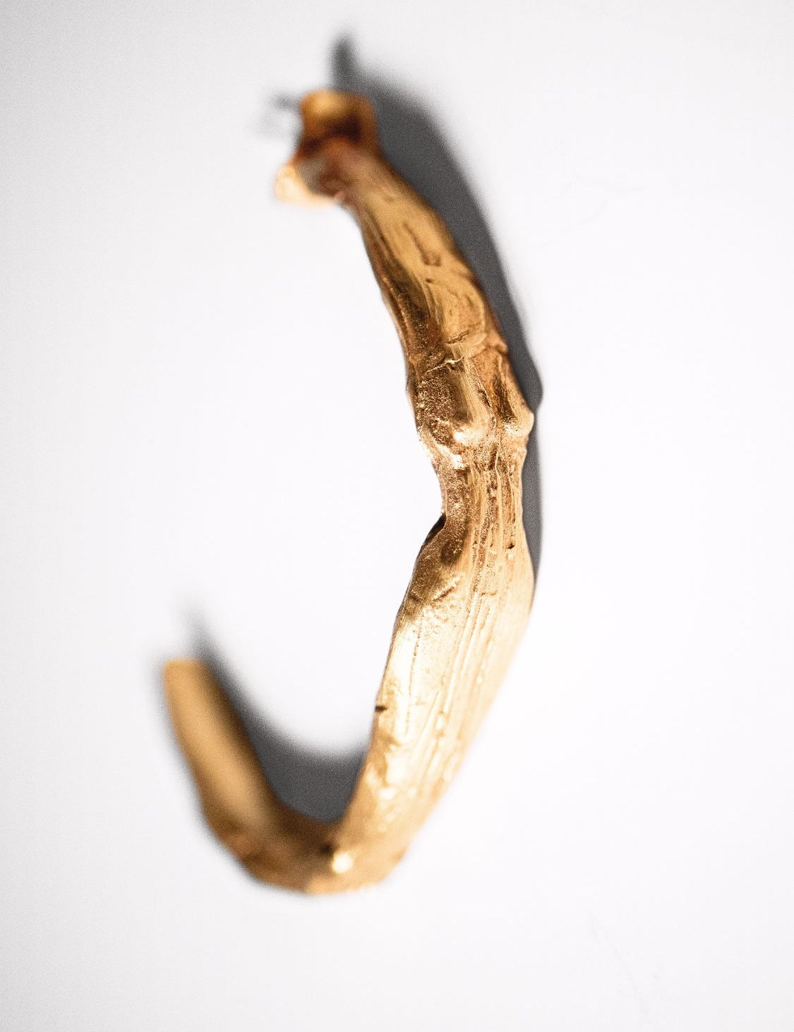 Gold-colored sculptural goddess hoops on a white background