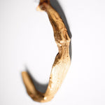 Gold-colored sculptural goddess hoops on a white background