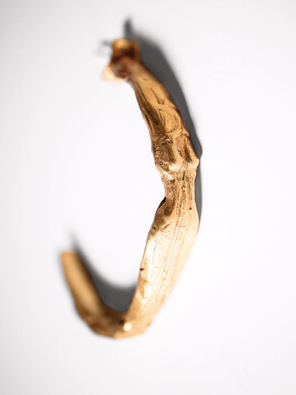 Gold-colored sculptural goddess hoops on a white background